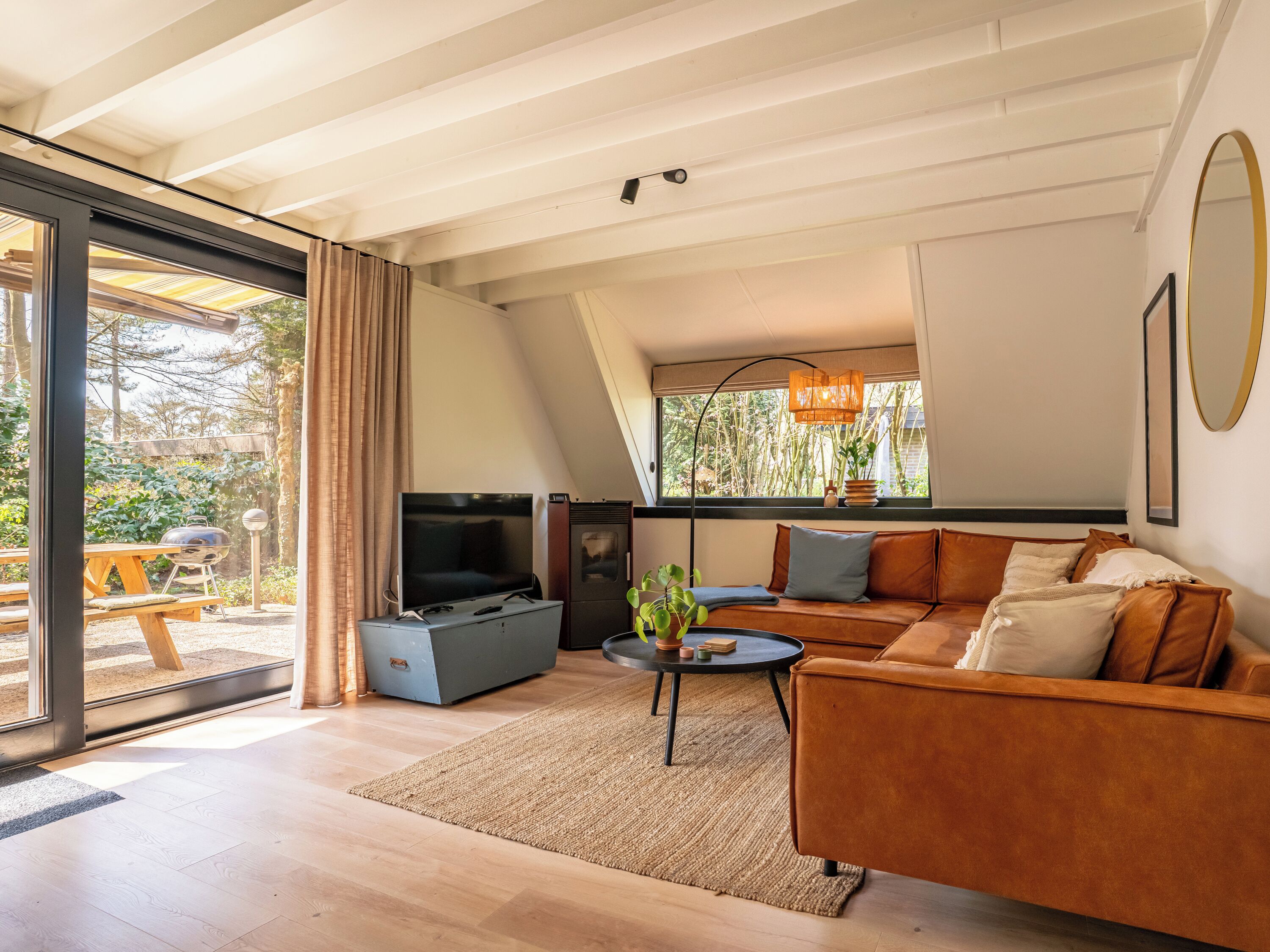 A modern living room with a TV, sofa, and a dining area visible through glass doors.