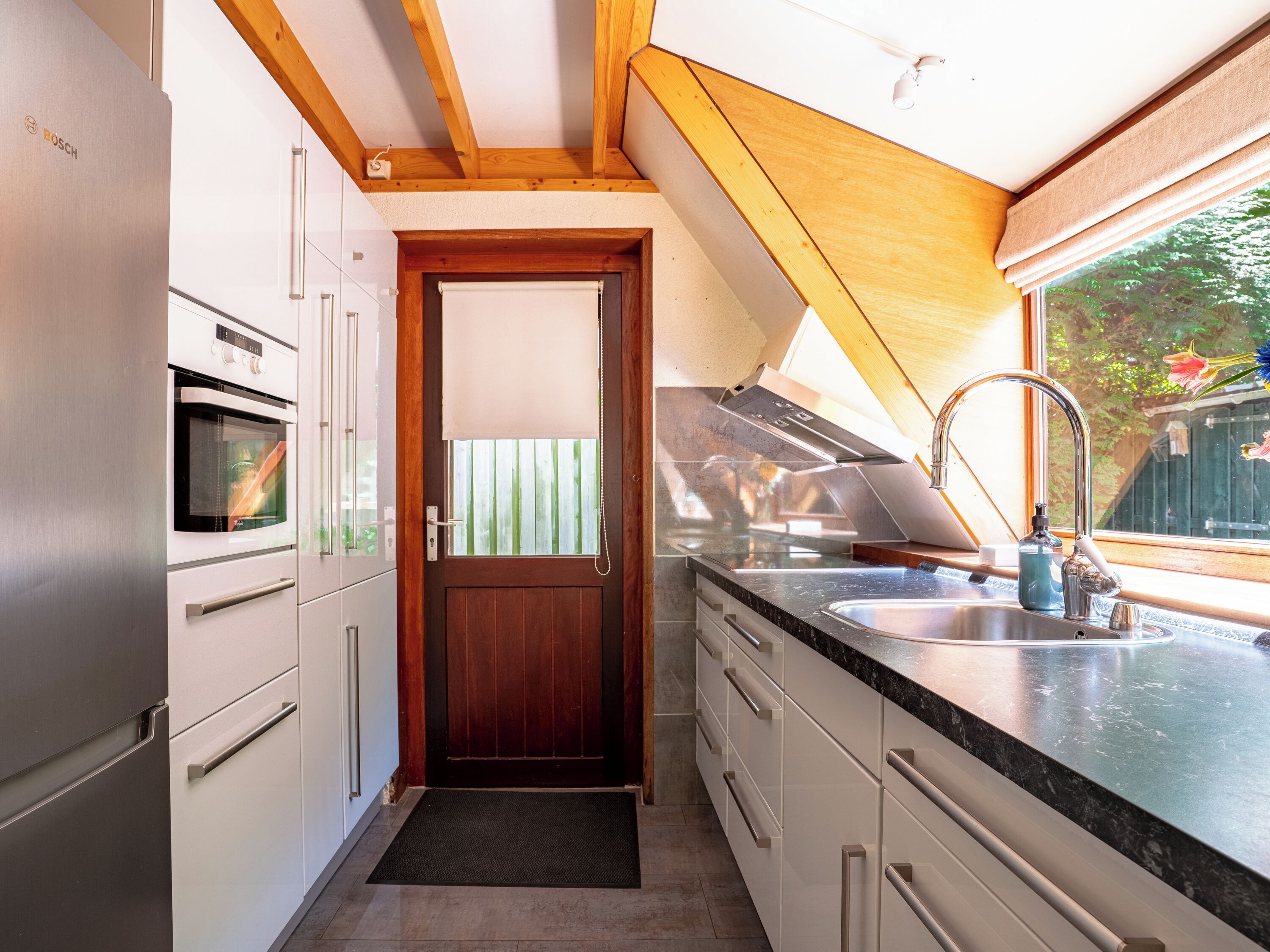 Una cocina compacta con un refrigerador Bosch, horno y una puerta de madera.