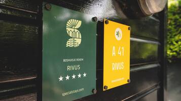Two signs on a bench: one green with a logo and text 'BOSHUISJE REKEM RIVUS' and a website 'specialstays.com', and one yellow with 'A 41 RIVUS' and a website 'www.rivus.com'.