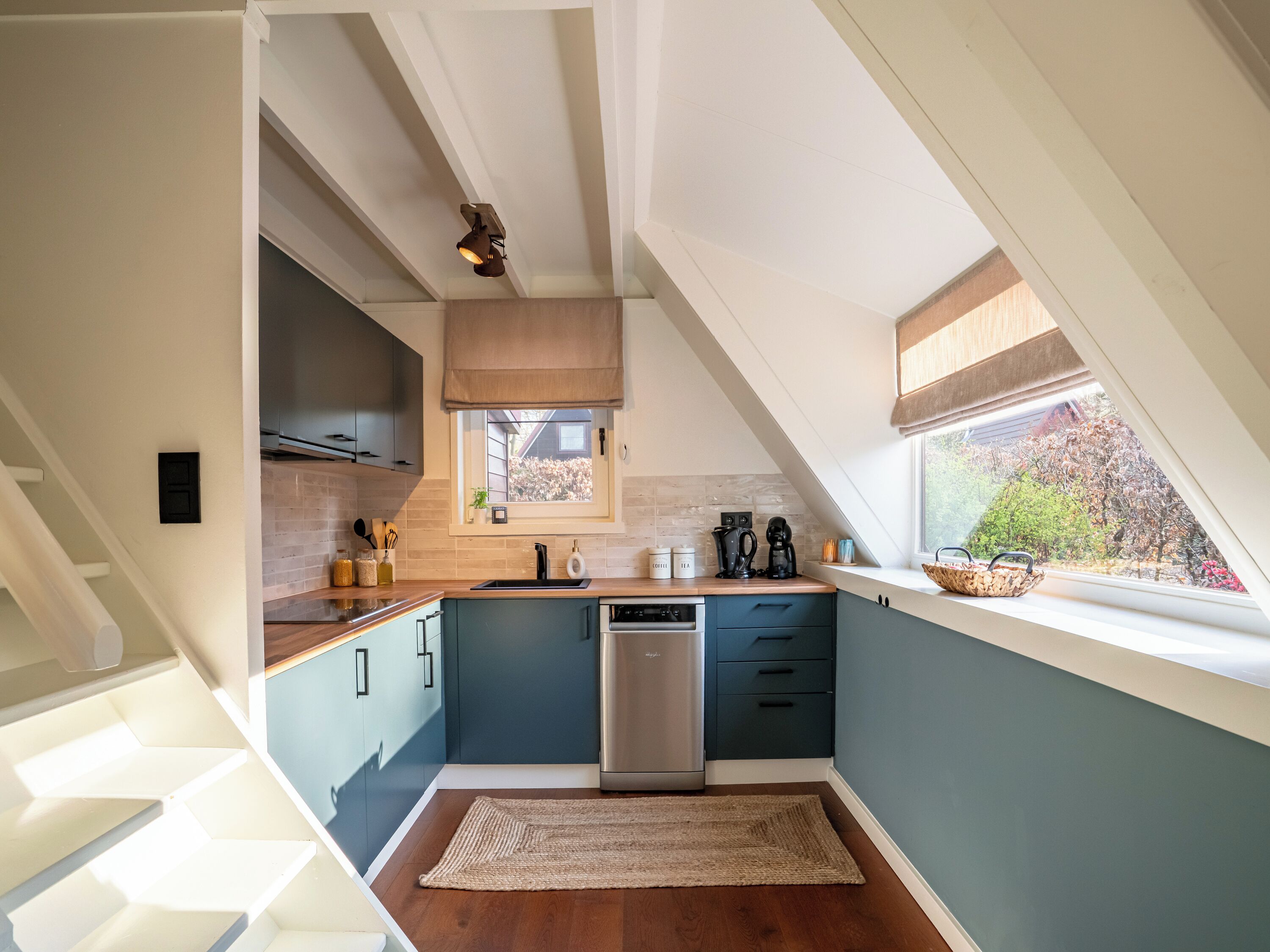 Una cocina moderna con techo inclinado, armarios empotrados, lavavajillas y ventana con vistas al exterior.