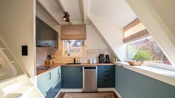Una cocina moderna con techo inclinado, armarios empotrados, lavavajillas y ventana con vistas al exterior.