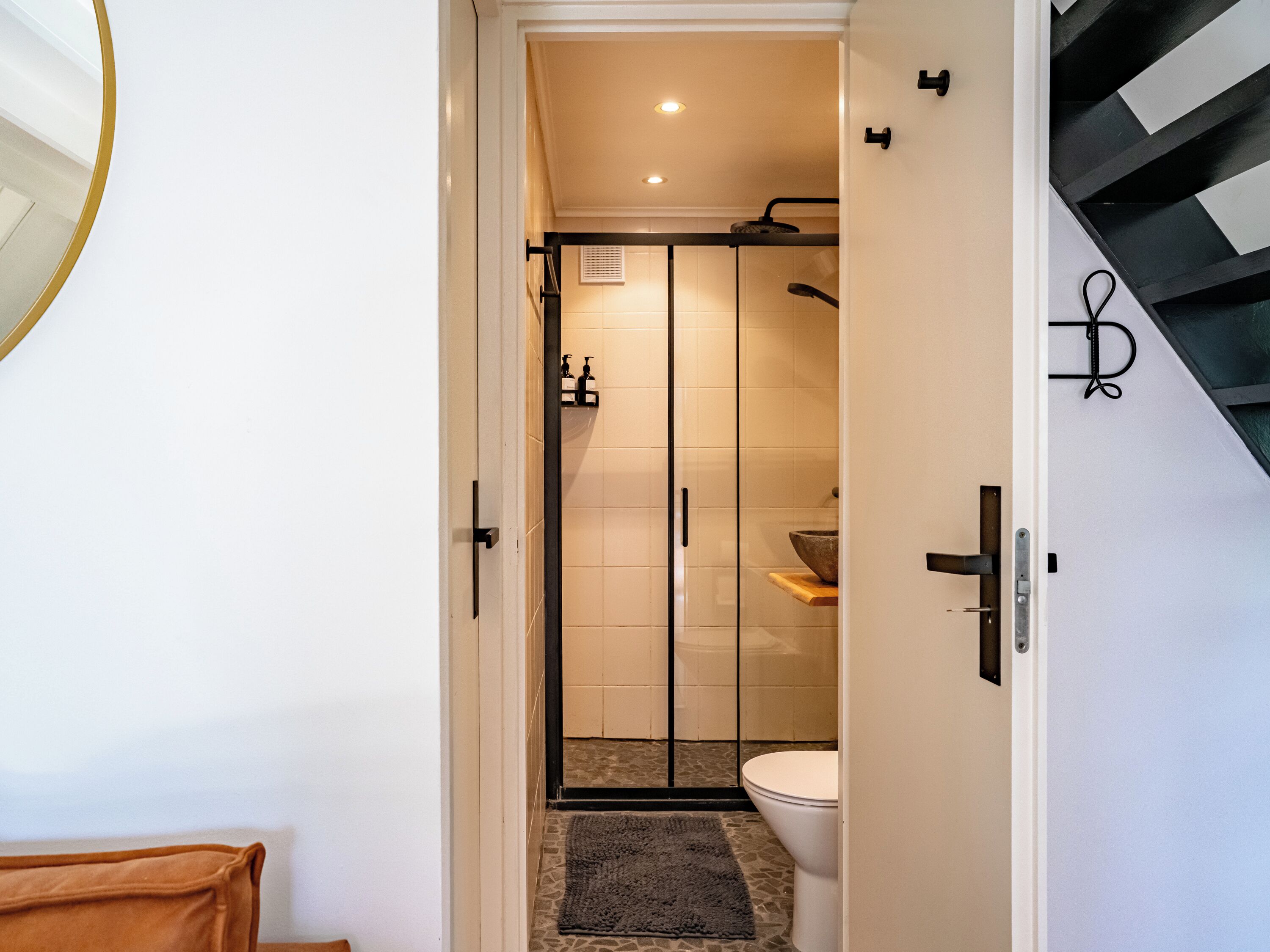 A modern bathroom with a glass shower enclosure, a white toilet, and a small sink area.