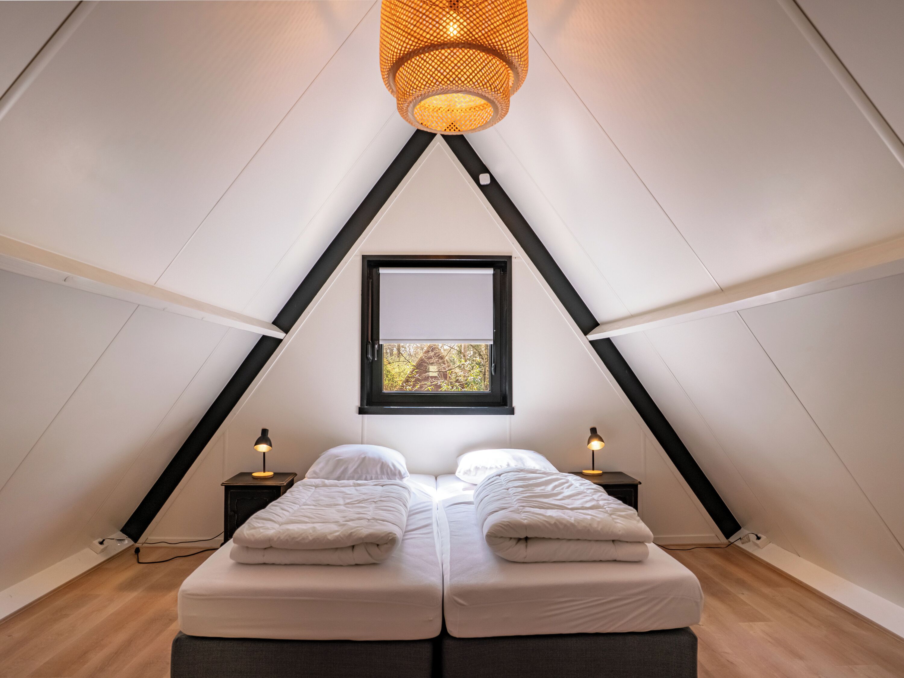 Een knus slaapkamer op zolder met een schuine kap, twee bedden, een raam met uitzicht en een hangende lamp.