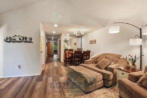 A spacious living room with a sofa set, a dining area, and a hallway leading to a kitchen.