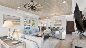 A spacious living area with a modern ceiling fan, a dining table with chairs, and a flat-screen TV mounted on the wall. - 5BR Home w/ private heated pool, golf cart, near 30A! (Santa Rosa Beach)