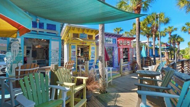 A colorful outdoor seating area with wooden chairs and tables, surrounded by buildings with various shops and signs. - 5BR Home w/ private heated pool, golf cart, near 30A! (Santa Rosa Beach)