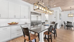 A modern kitchen with white cabinets, a stainless steel refrigerator, and a central island with chairs. - 5BR Home w/ private heated pool, golf cart, near 30A! (Santa Rosa Beach)