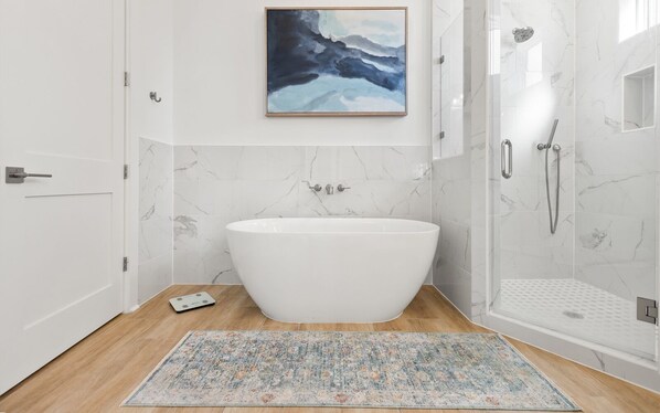 A modern bathroom with a freestanding bathtub, a shower, and a marble-tiled wall.