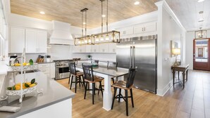 A modern kitchen with white cabinetry, a stainless steel refrigerator, and a central island with chairs.