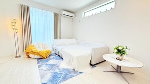 Quarto de hotel moderno com uma cama, uma mesinha redonda com uma planta, um abajur e uma janela grande com cortinas.