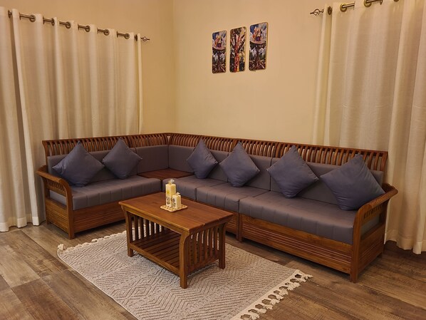 A L-shaped sectional sofa with cushions, a wooden coffee table, and a patterned rug in a room with curtains and wall art.