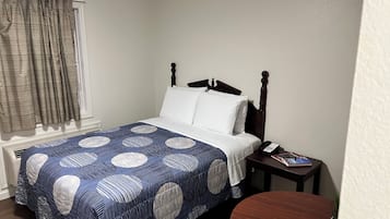 A neatly made bed with a blue and white patterned bedspread, a wooden headboard, and a bedside table with a phone and a book.