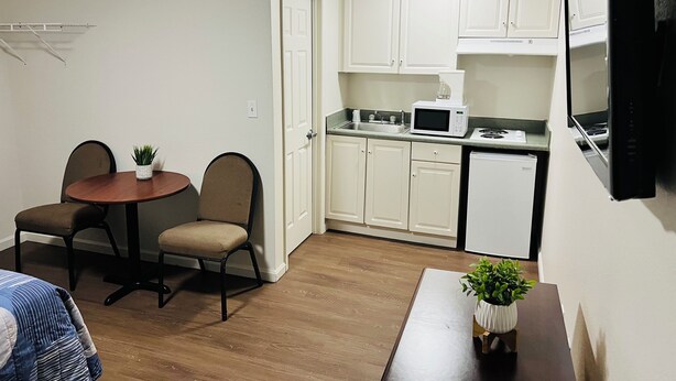 A compact kitchen with white cabinets, a microwave, a sink, and a dishwasher. There is a dining area with a round table and two chairs. - Stay Lodge Decatur (Decatur)