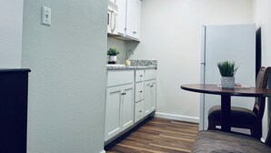 A compact kitchen with white cabinets, a wooden countertop, and a small dining table with a chair. - Stay Lodge Decatur (Decatur)