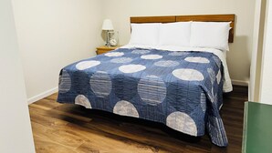 A neatly made bed with a blue and white patterned bedspread, a wooden headboard, and a small bedside table with a lamp and clock. - Stay Lodge Decatur (Decatur)