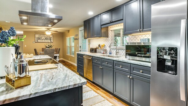 A modern kitchen with dark cabinetry, a stainless steel refrigerator, and a marble countertop. - Lakefront Home w/ Hot Tub & Dock in Orlando! (Orlando)