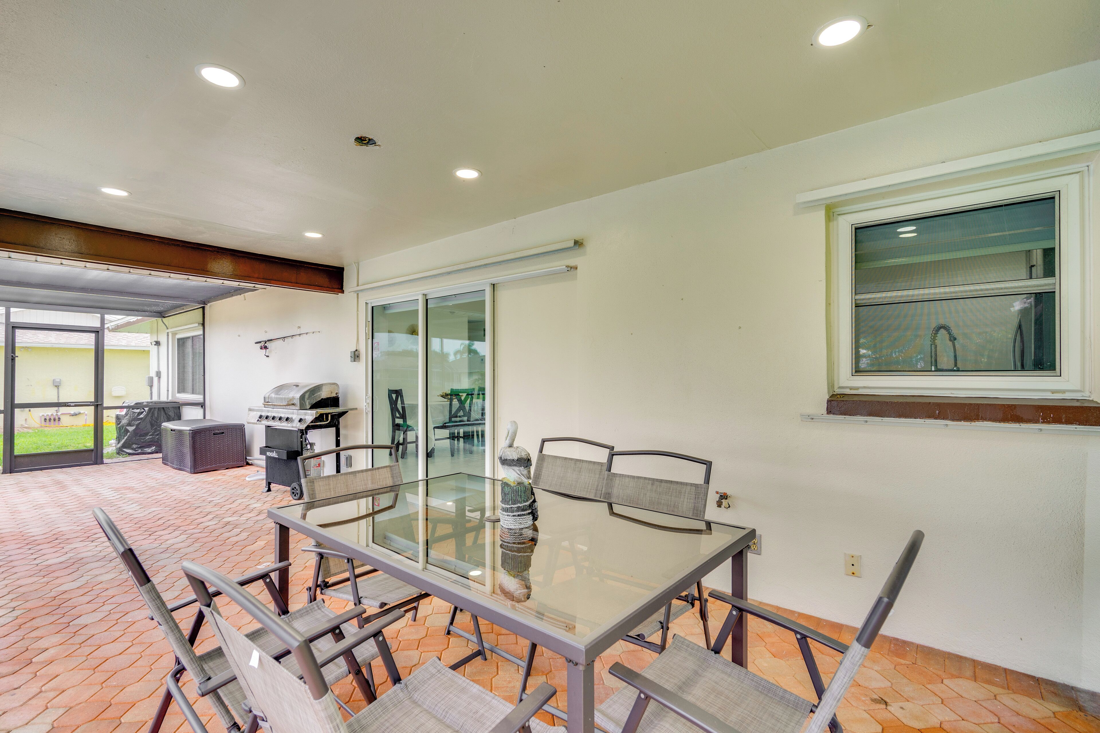 A spacious patio with a glass-top table and chairs, a grill, and a view of the outdoors.
