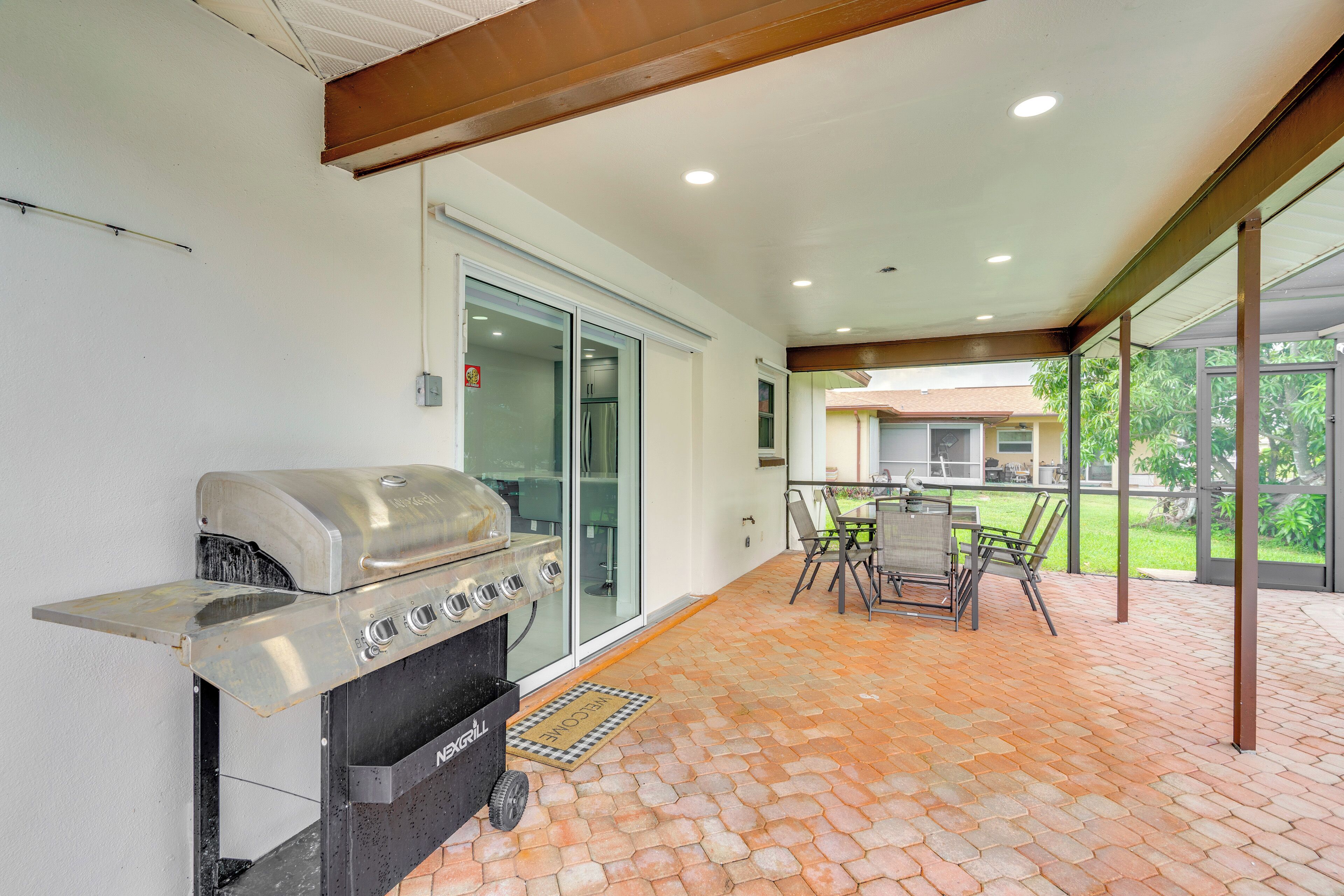 An outdoor patio with a barbecue grill, a dining table with chairs, and a view of a house through large glass doors.