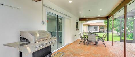 An outdoor patio with a barbecue grill, a dining table with chairs, and a view of a house through large glass doors.