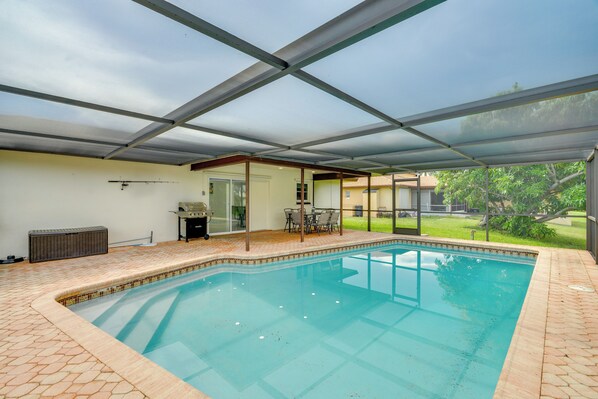 A swimming pool with a glass enclosure, a patio area with outdoor furniture, and a view of a residential area. - Swim, Golf & Explore: Pet-friendly Cape Coral Home (Cape Coral)
