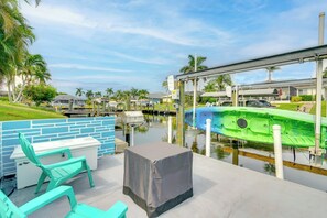 A waterfront patio with a covered table, chairs, and a kayak docked by the water. - Swim, Golf & Explore: Pet-friendly Cape Coral Home (Cape Coral)
