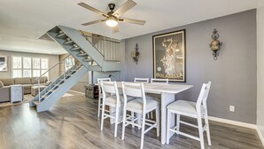 A spacious living area with a staircase, a dining table with chairs, and a ceiling fan.