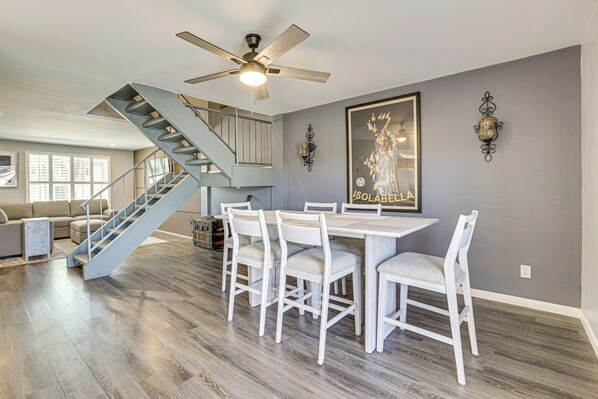 Un vaste espace de vie comprenant un escalier, une table à manger avec des chaises et un ventilateur de plafond.