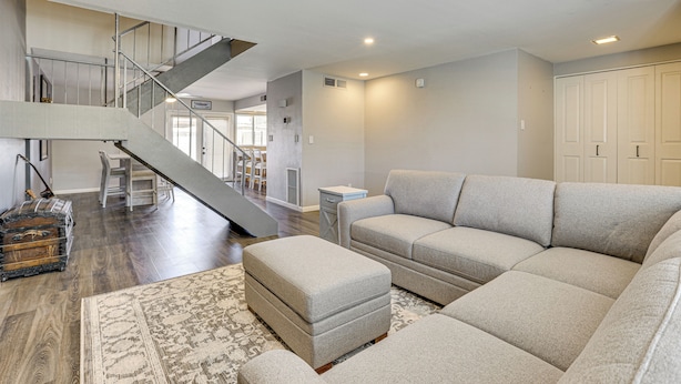 A spacious living room with a large sectional sofa, a small ottoman, a patterned rug, and a staircase leading to an upper level.