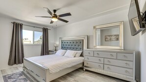 A bedroom with a bed, a dresser, a ceiling fan, a window with curtains, and a rug.