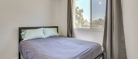 Un dormitorio con cama, ventana y cortinas.