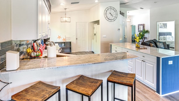 A modern kitchen with a marble countertop, wooden stools, and a clock on the wall. - Golf & Hike: Family Home in Rotonda West! (Rotonda West)