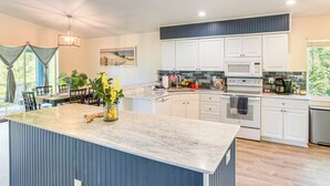 A modern kitchen with white cabinets, a large island with a marble countertop, and a view of the outdoors. - Golf & Hike: Family Home in Rotonda West! (Rotonda West)