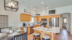 A modern kitchen with wooden cabinets, a central island, and a dining area with chairs and a table set for four. - 1 Mi to Golf Course: Yuma Oasis w/ Furnished Patio (Yuma)