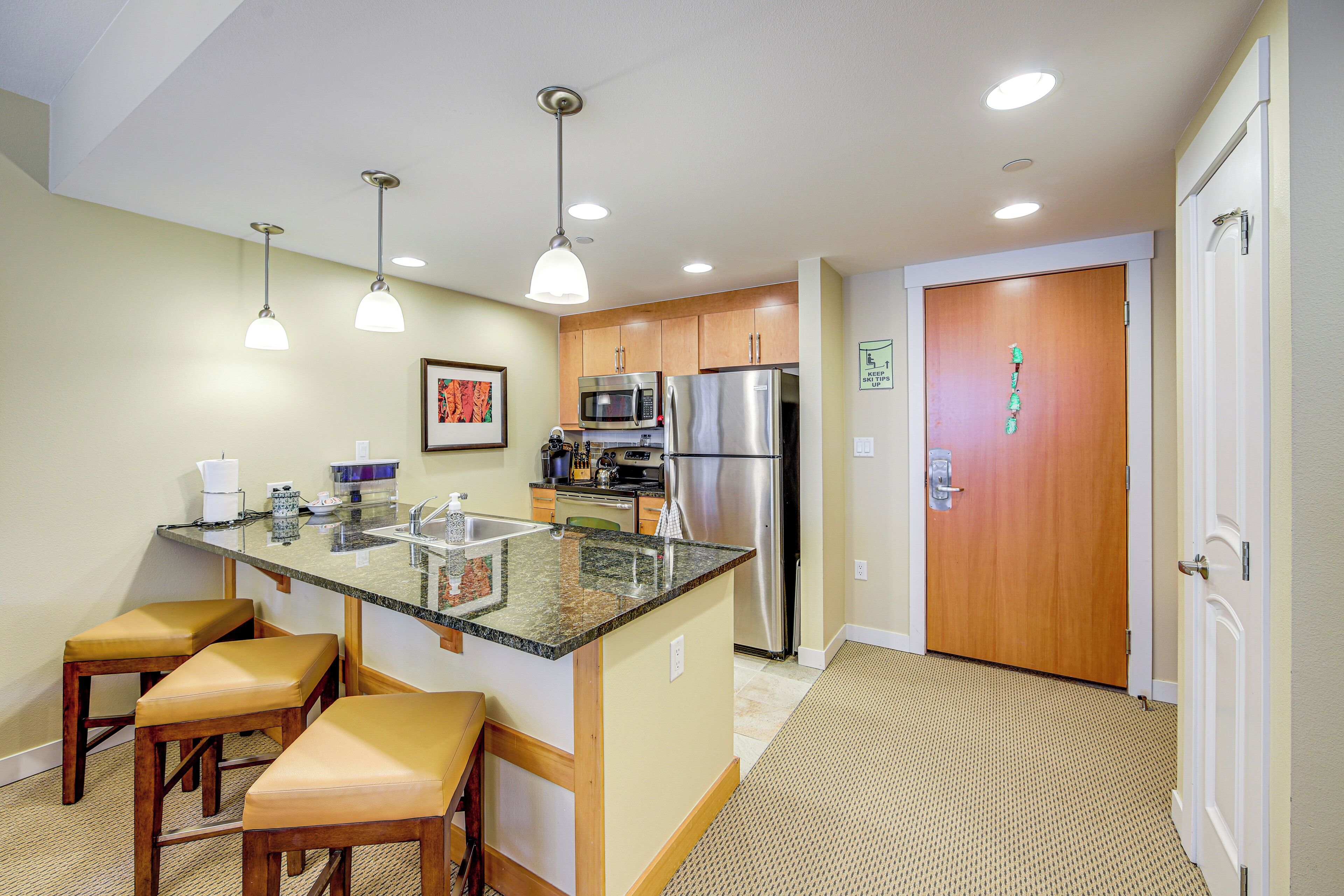 Una cocina compacta con isla central, electrodomésticos de acero inoxidable e iluminación colgante.