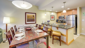 A modern kitchen with stainless steel appliances, a dining area with a long table set for six, and pendant lighting. - 100 Steps to Gondola: Cozy Winter Park Condo! (Winter Park)