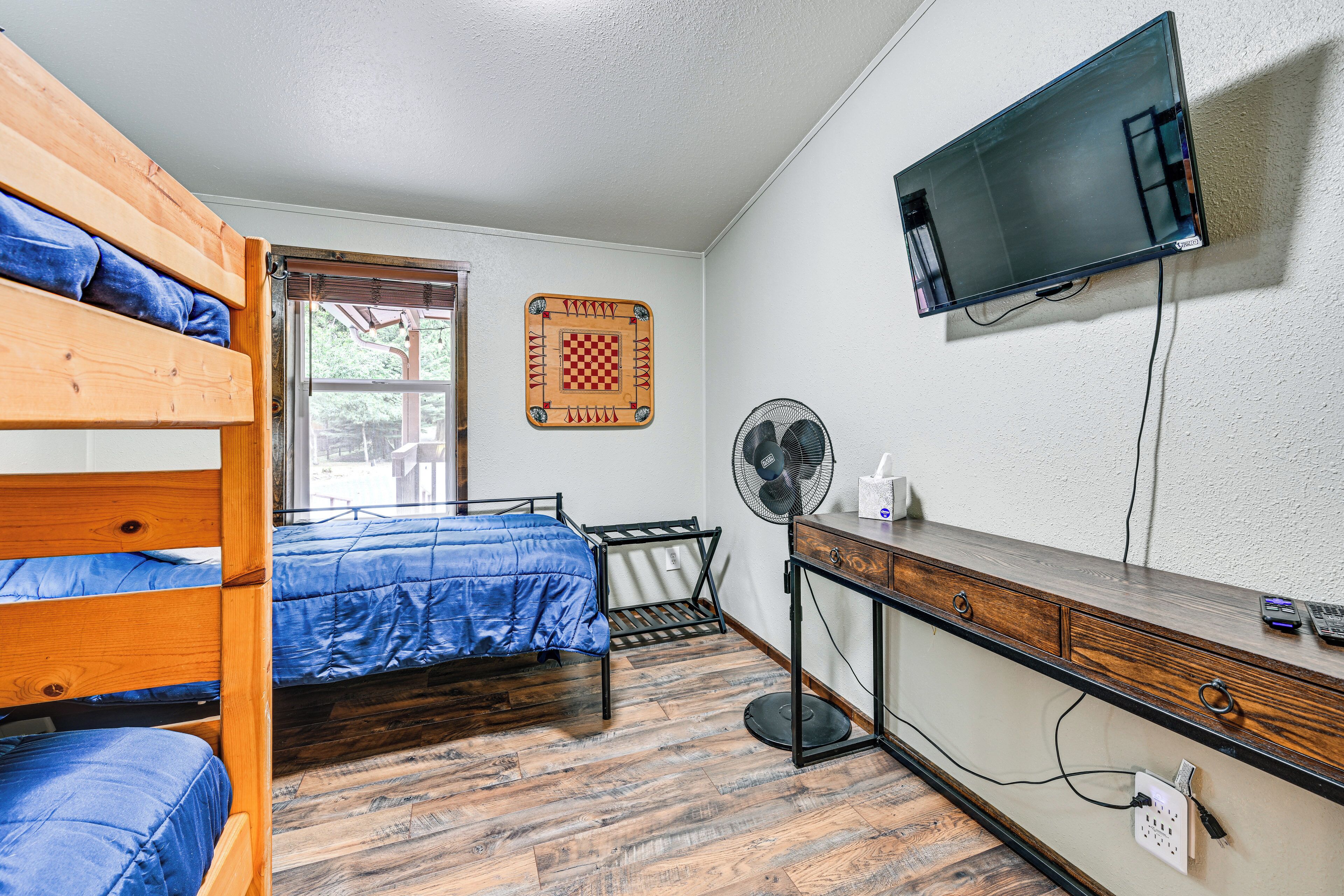 A room with a bunk bed, a desk with a computer, a wall-mounted TV, and a fan.