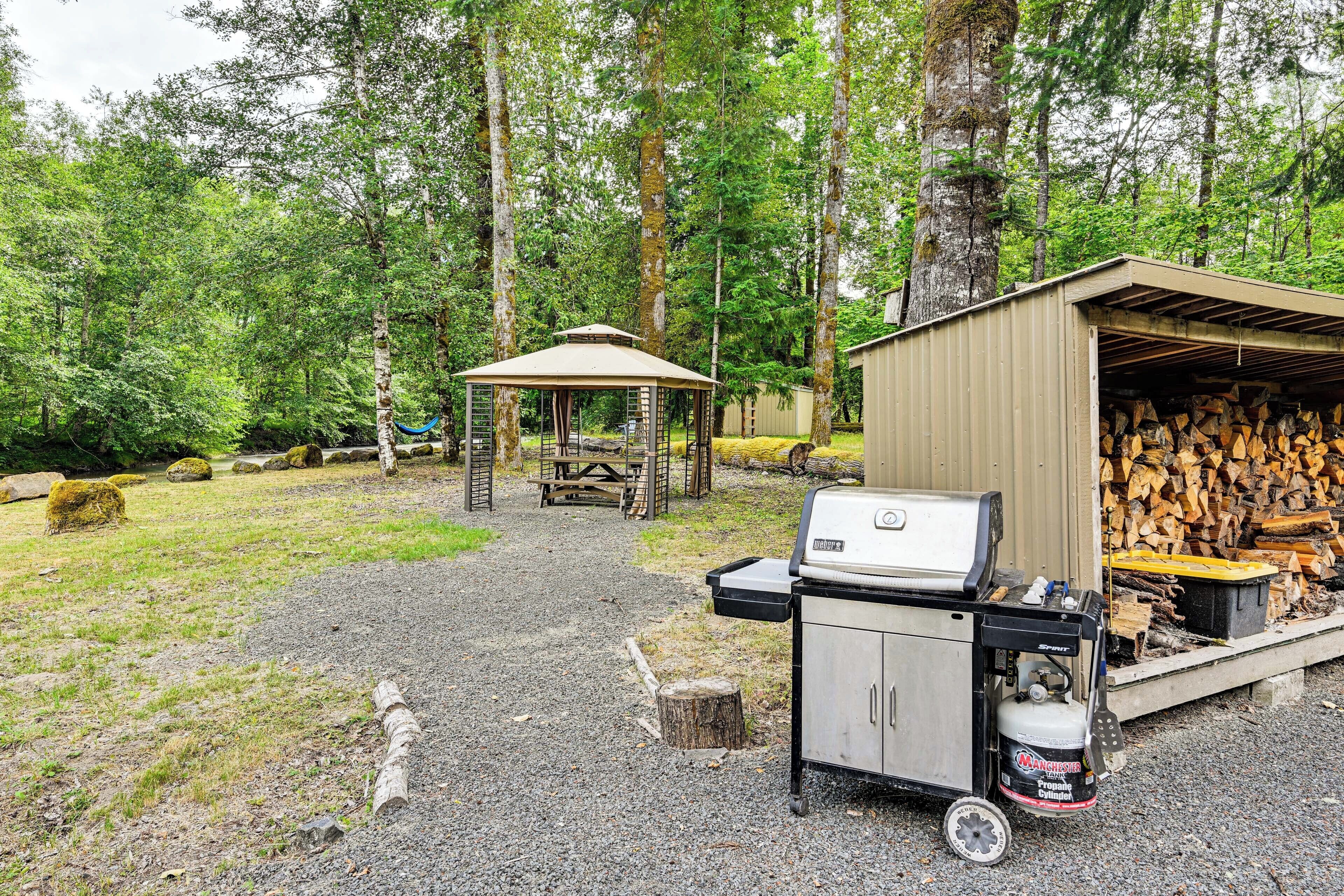 Un área de camping con una parrilla, un cobertizo para leña y una mesa de picnic cubierta.