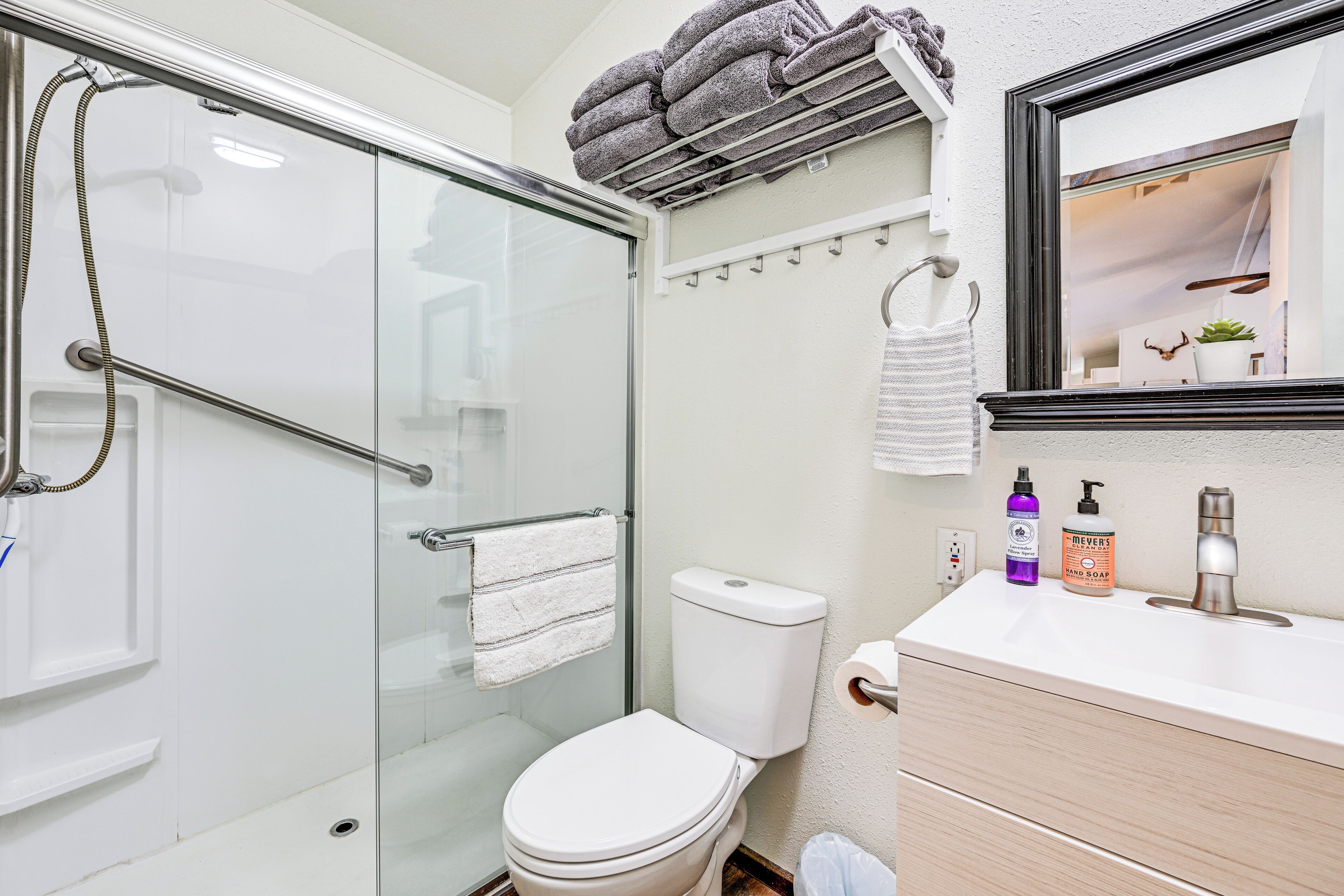 A modern bathroom with a glass shower enclosure, a toilet, a sink with toiletries, and a towel rack with towels.
