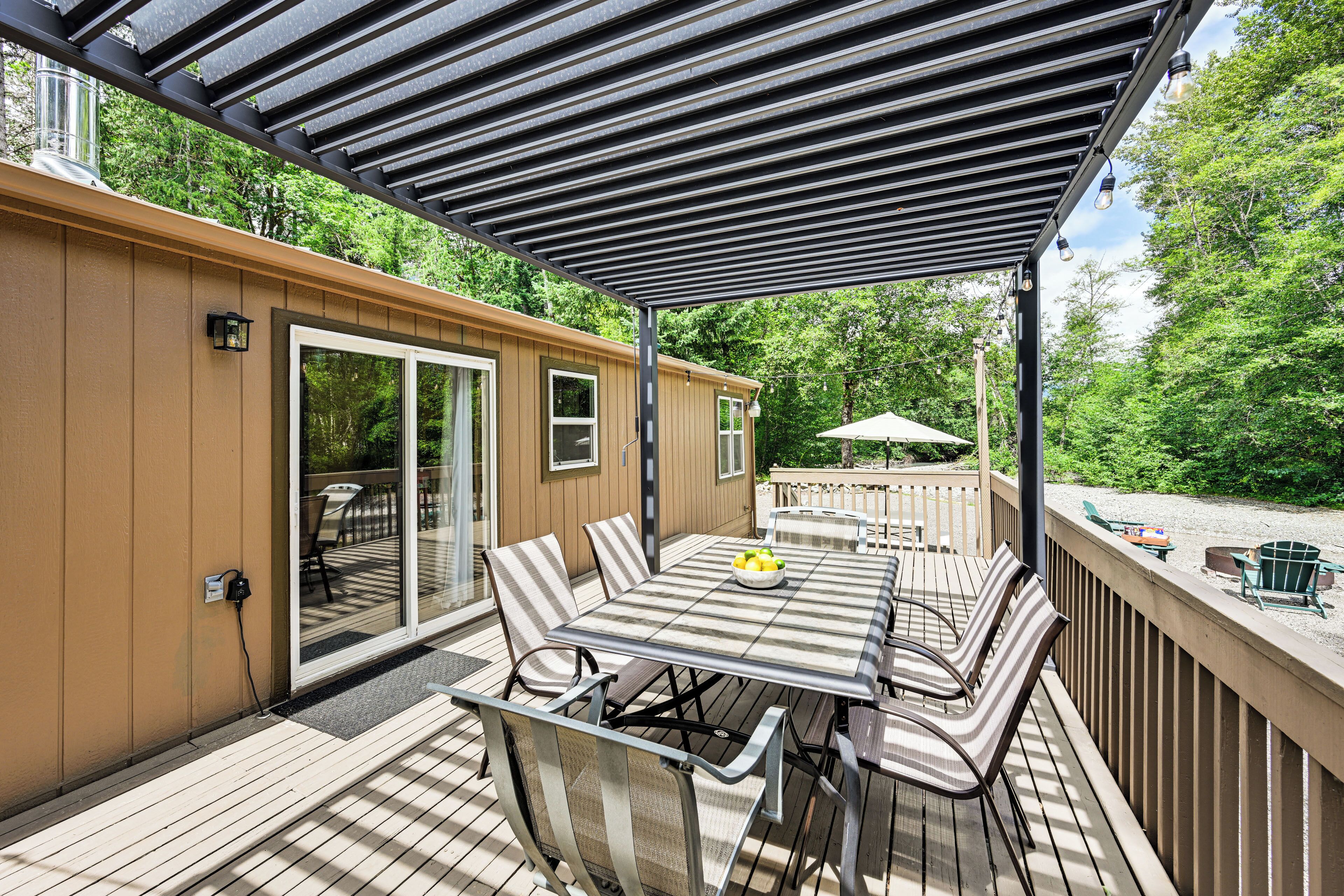 A covered outdoor deck with a table and chairs, a power outlet, and a view of the backyard.
