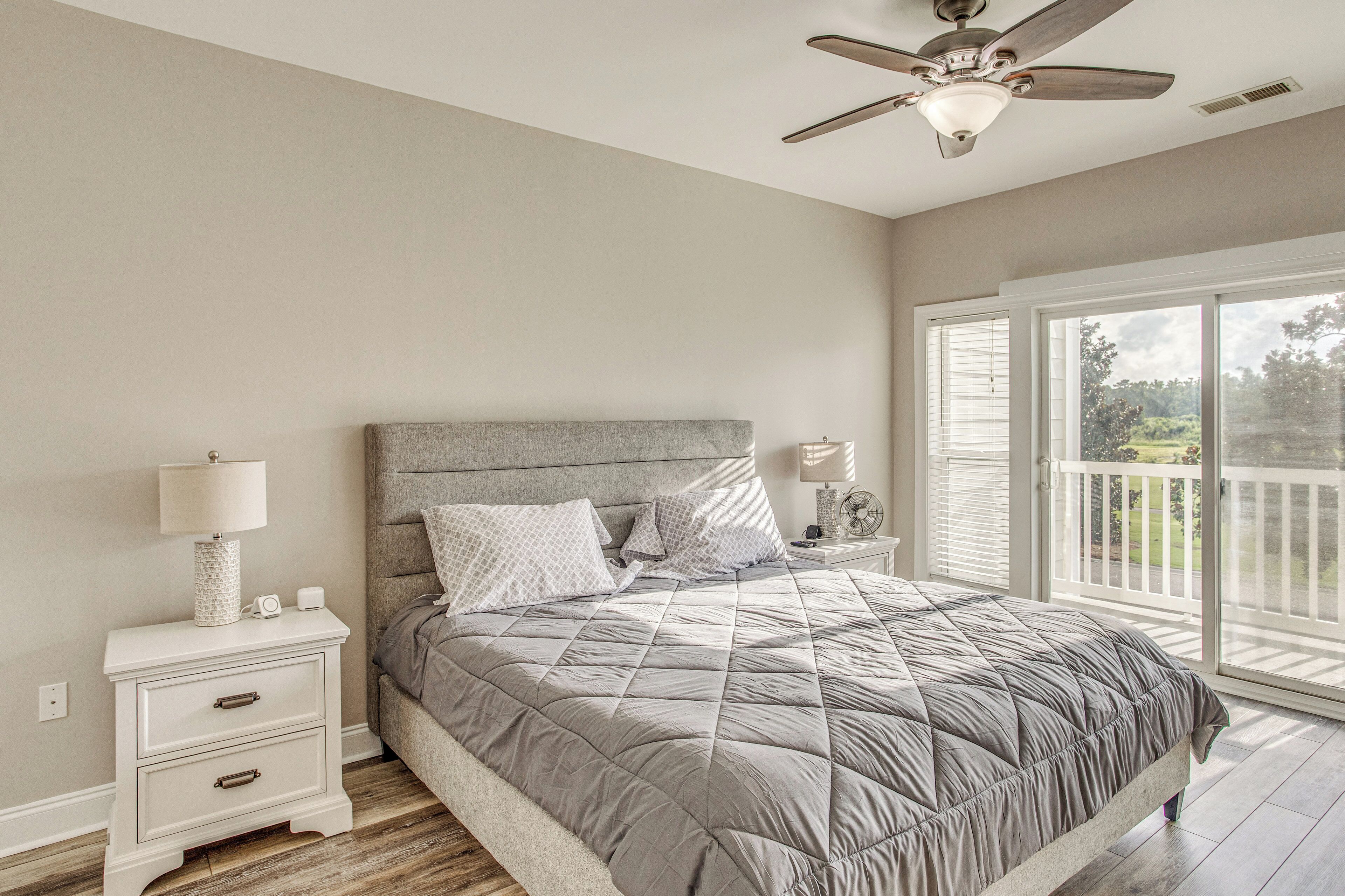 Une chambre à coucher avec un lit, des tables de chevet, un ventilateur de plafond et une vue sur l’extérieur.