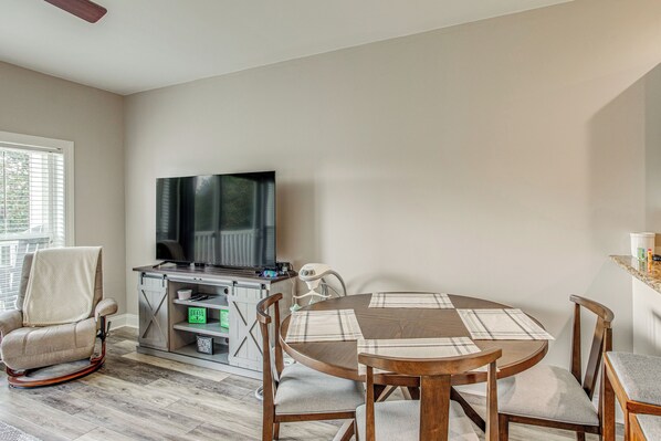 A living room with a television, a dining table with chairs, and a window with blinds. - Tee Off & Unwind By Pool: Myrtle Beach Condo (Myrtle Beach)