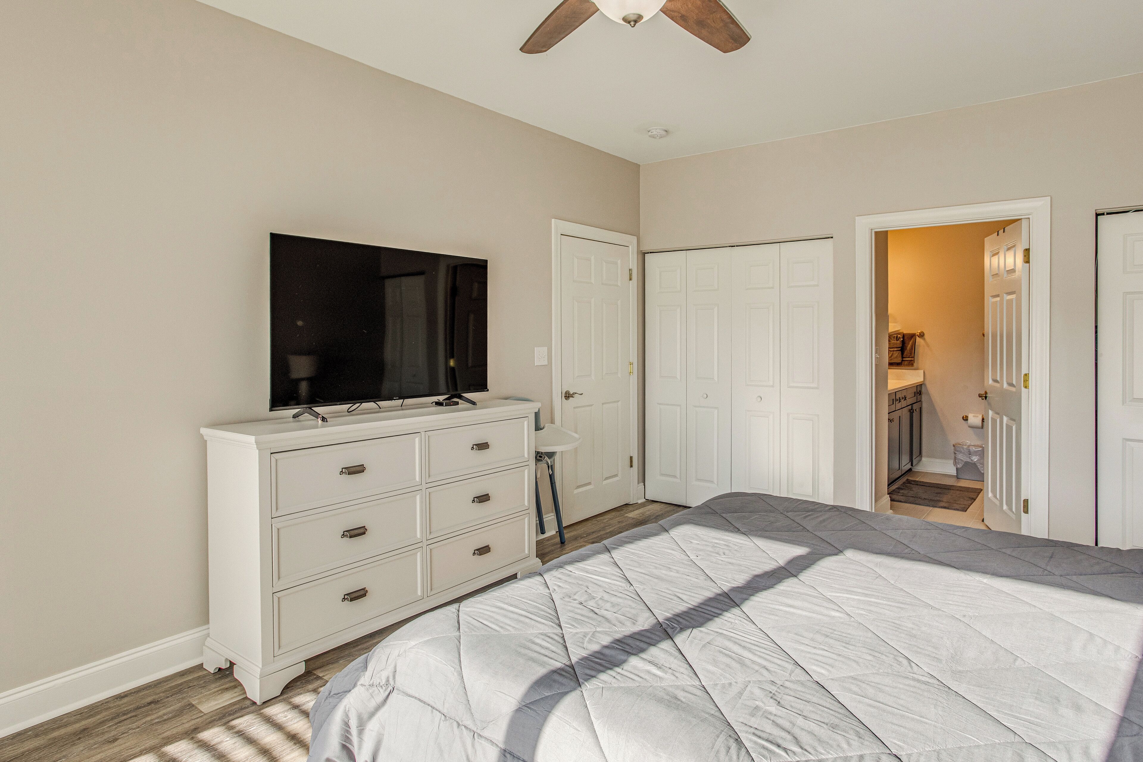 A bedroom with a bed, a dresser, a TV, and a ceiling fan.