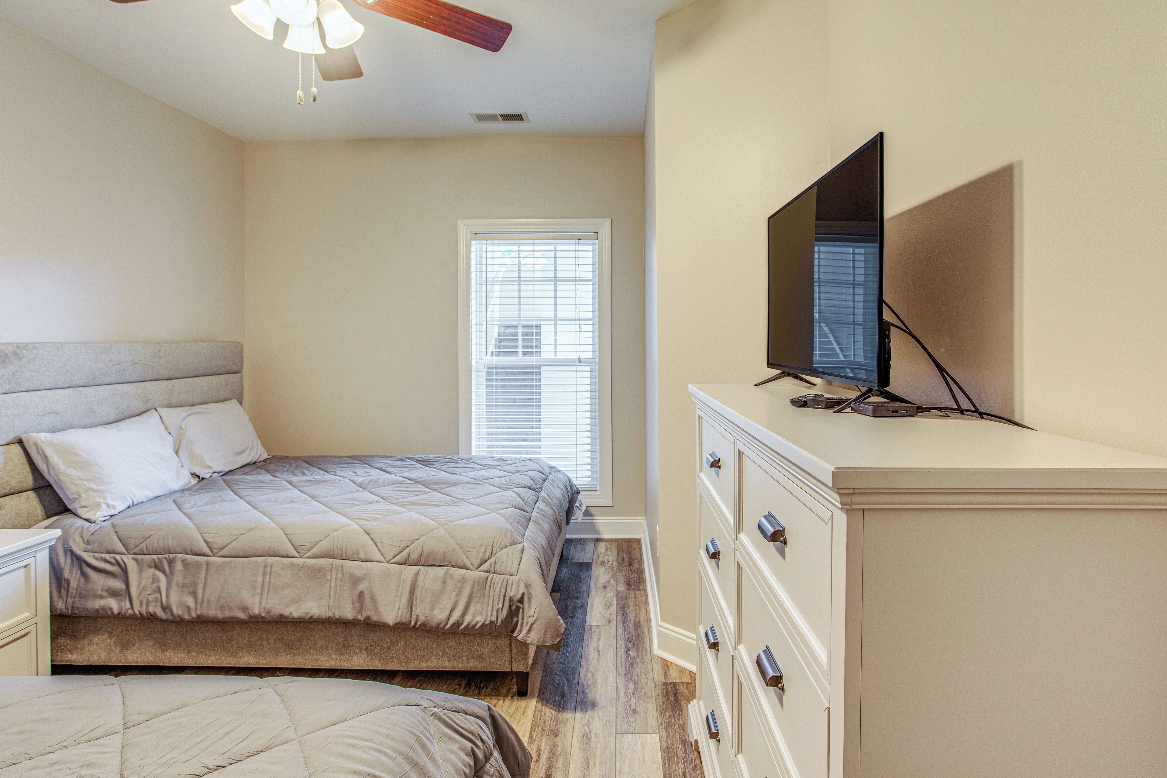 A bedroom with a bed, dresser, TV, and a window with blinds.