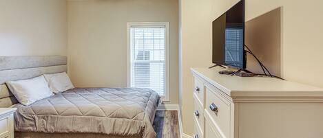 A bedroom with a bed, dresser, TV, and a window with blinds.