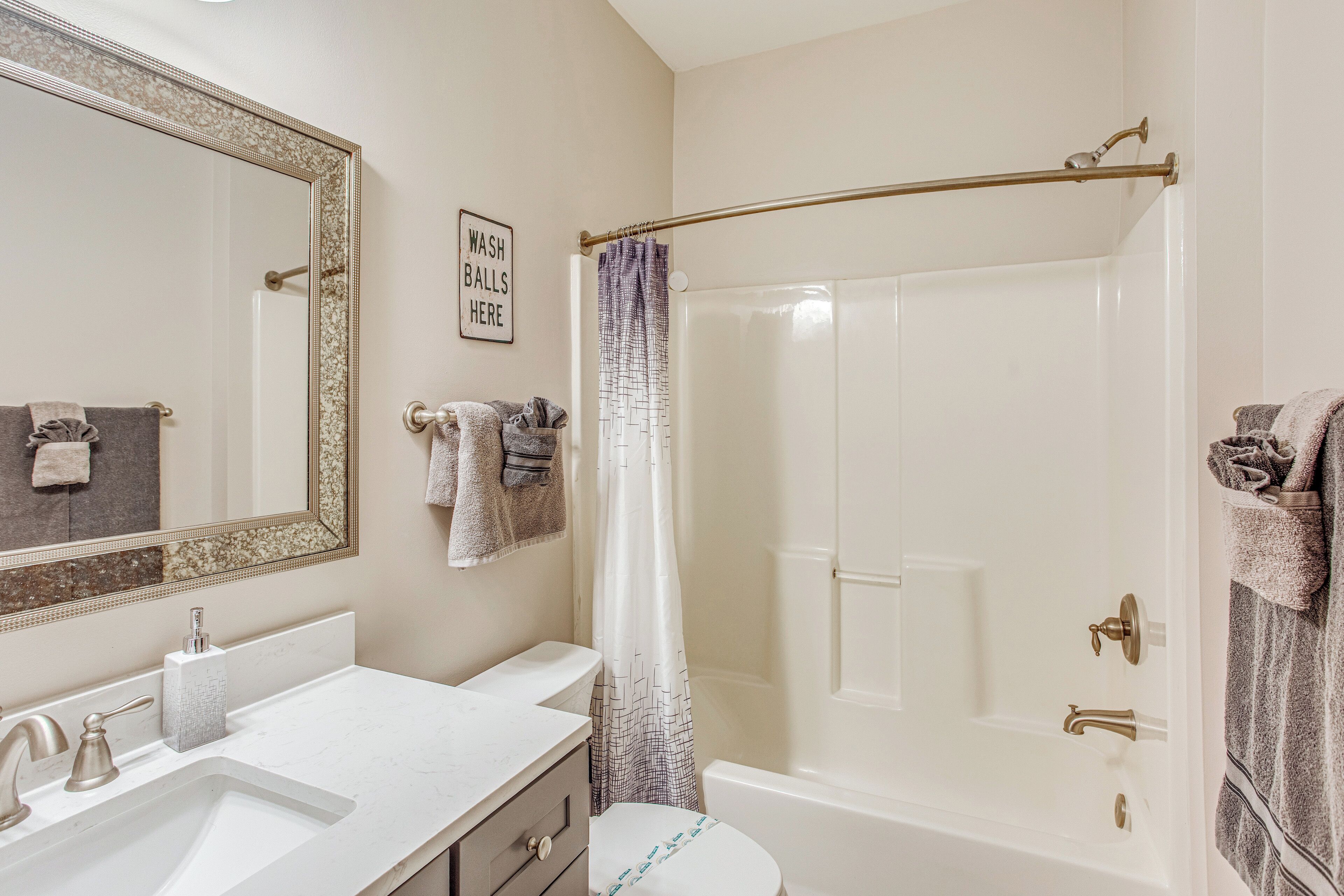 A bathroom with a white sink, a mirror with a decorative frame, a shower curtain, and a sign that says "WASH BALLS HERE".