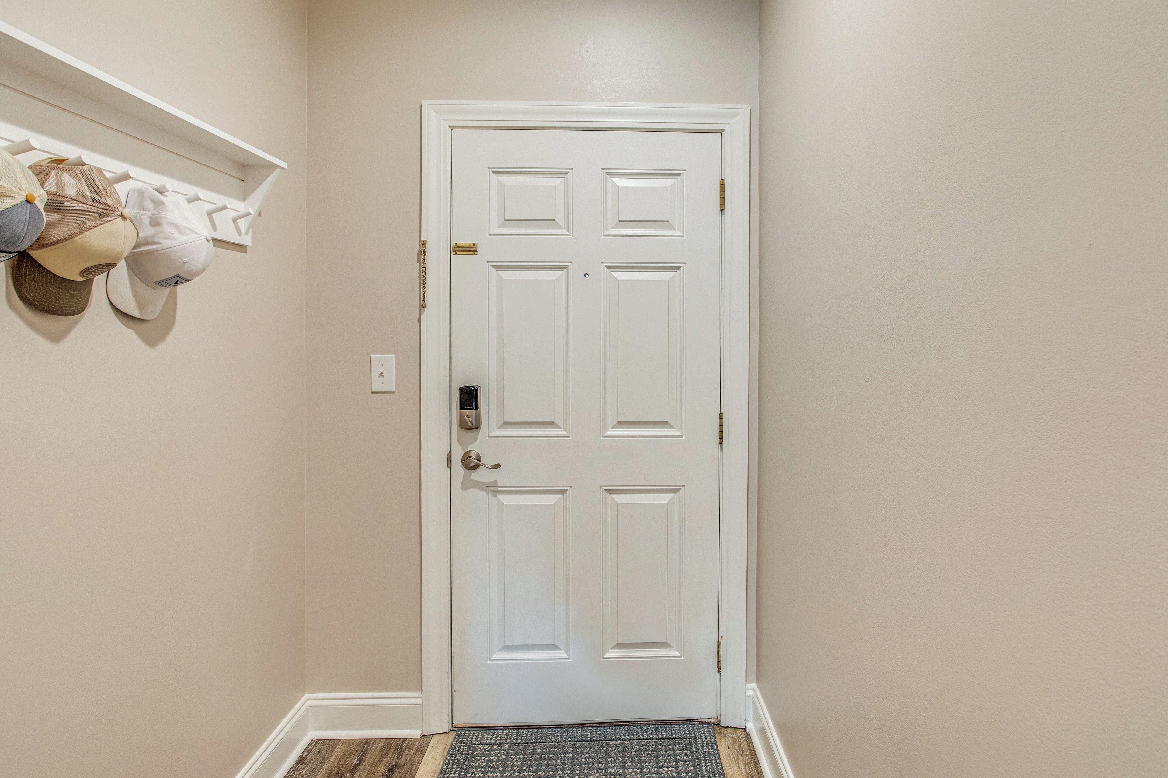 A white door with a keypad lock, a doormat, and a wall-mounted hat rack with several hats.