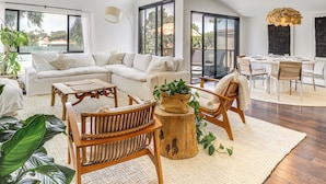 A spacious living area with a large sectional sofa, wooden chairs, a coffee table, and a dining table with chairs. There is a large window providing a view of the outdoors. - Resort Perks, Ocean Access: Solana Beach Townhome! (Solana Beach)