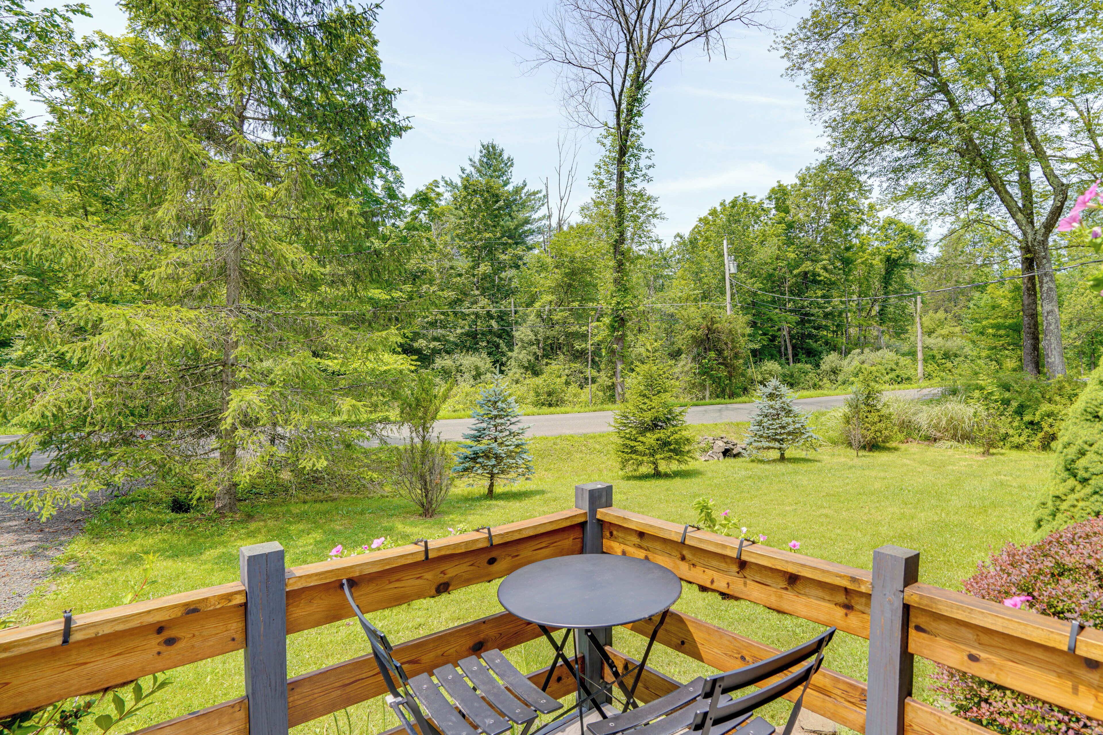 A wooden deck with a table and chairs, surrounded by lush greenery and trees.