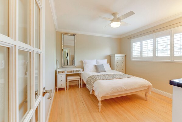 Une chambre à coucher comprenant un lit, un bureau, une chaise, une commode et un ventilateur de plafond.