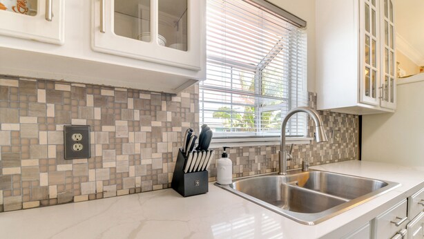 Una cocina con salpicadero de azulejos, un lavamanos de acero inoxidable y armarios blancos.